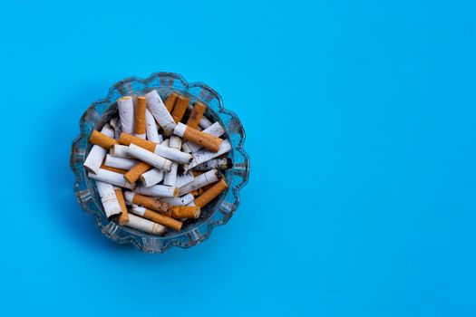 Cigarette butts in glass ashtray on blue background.