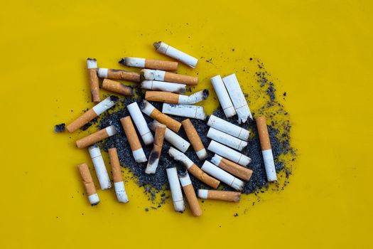 Cigarette butts and ash on yellow background.