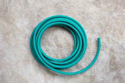 Green garden hose on cement floor background.