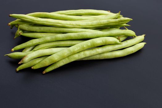Pile of green bean pods on dark background.