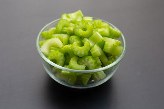 Fresh celery slices in glass bowl on dark background. 