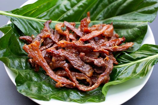 Deep fried sun-dried pork on noni or morinda citrifolia leaf on dark background.