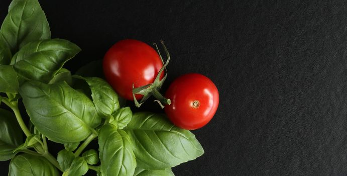 Fresh cherry tomatoes on black background, green basil. Top view, copy space