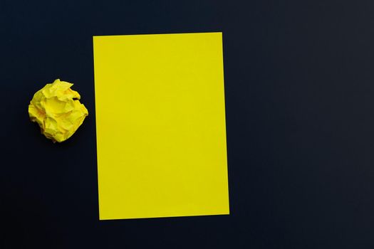 Yellow sheet with crumpled paper ball on dark background. Copy space