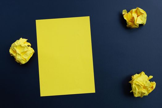 Yellow sheet with crumpled paper balls on dark background. Copy space