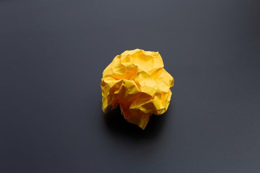 Crumpled yellow paper ball on dark background. Copy space