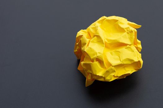 Crumpled yellow paper ball on dark background. Copy space