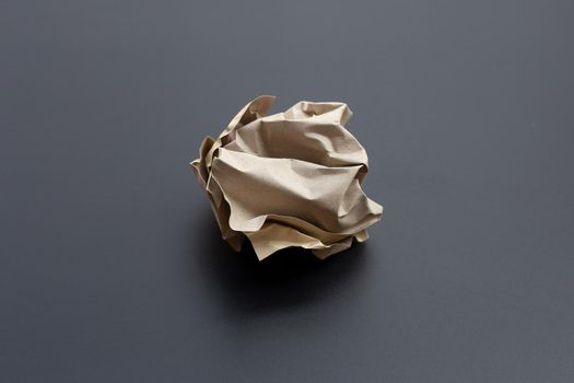 Crumpled brown paper ball on dark background. Copy space