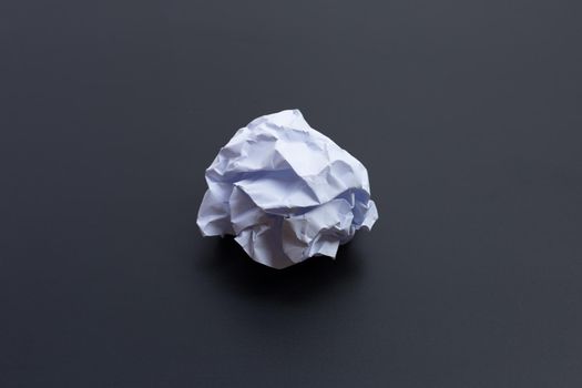 Crumpled white paper ball on dark background. Copy space