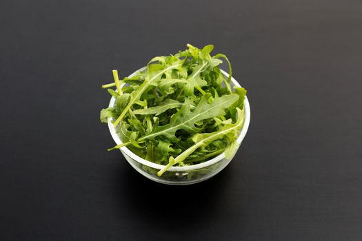 Fresh green rocket salad in glass bowl on dark background.