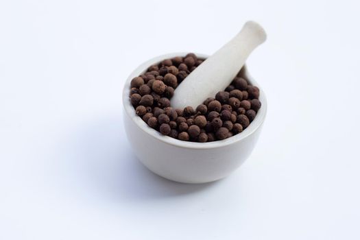 Allspice in porcelain mortar with pestle on white background. 