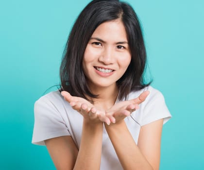 Portrait happy Asian beautiful young woman smile standing wear a white t-shirt, She blowing air kiss something on palms, studio shot on blue background with copy space for text