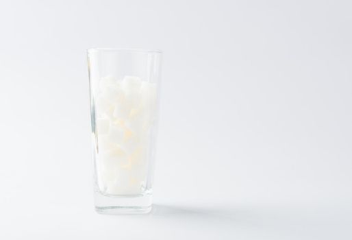 A glass full of white sugar cube sweet food ingredient, studio shot isolated on white background, health high blood risk of diabetes and calorie intake concept and unhealthy drink