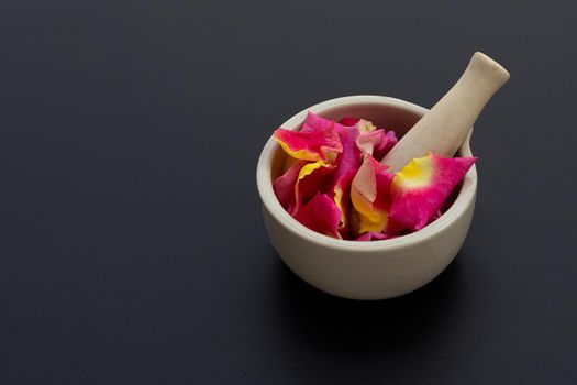 Rose petals in porcelain mortar with pestle isolated on dark background.
