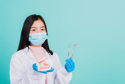 Asian beautiful woman dentist holding professional tool and model teeth denture, female doctor checking denture studio shot isolated on blue background. Dental hygiene surgery health care concept