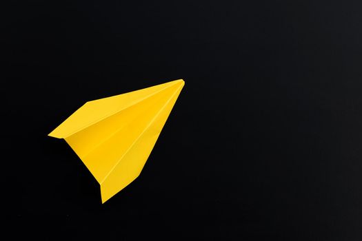 Yellow paper airplane on dark background. Top view
