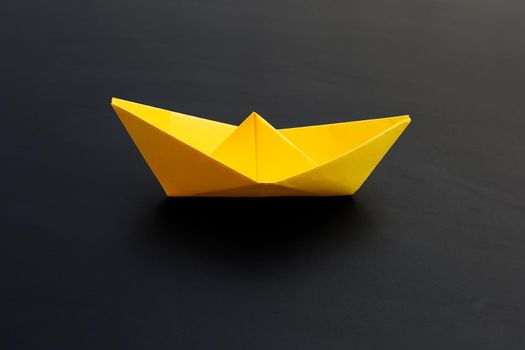 Yellow paper boat on dark background. Copy space