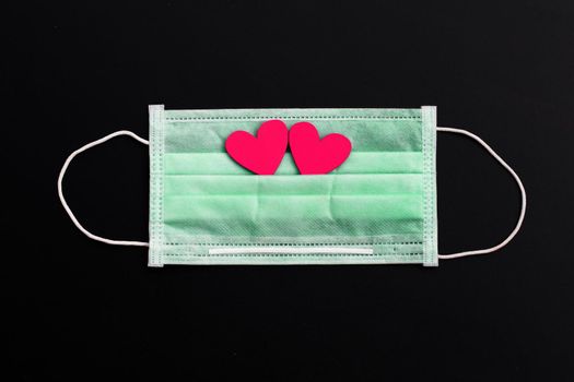Two pink wooden hearts on protective medical mask on dark background.