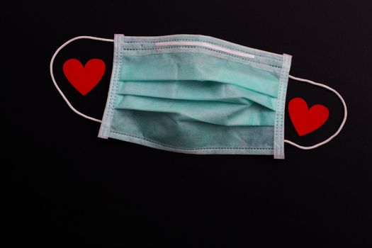 Two red wooden hearts on protective medical mask on dark background.