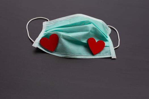 Two red wooden hearts on protective medical mask on dark background.