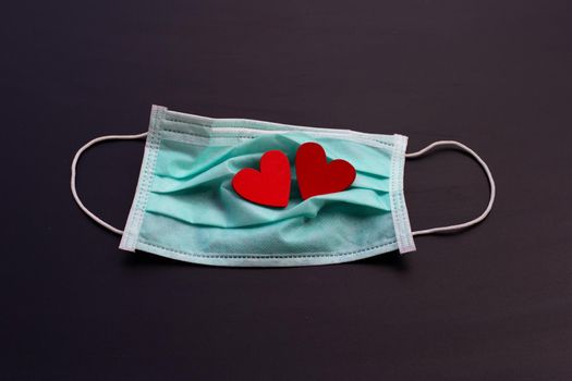 Two red wooden hearts on protective medical mask on dark background.