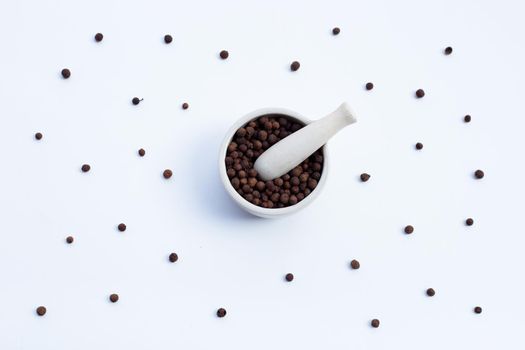 Allspice in porcelain mortar with pestle on white background.