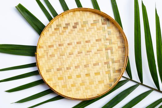 Empty wooden bamboo threshing basket on tropical palm leaves on white background.