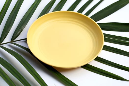 Empty yellow plate on tropical palm leaves on white background. 