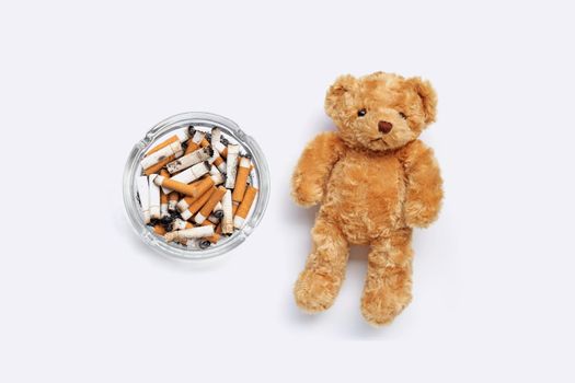 Brown teddy bear with cigarette butts and ashes on white background.