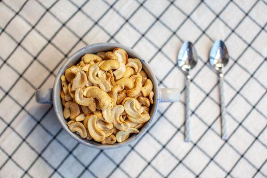 A plate of cashew nuts on a nice napkin and two spoons next to it. Delicious and healthy food for a snack. There is a place for the text.