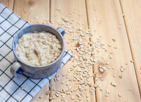 Fresh oatmeal porridge in a plate on a beautiful napkin and on a wooden table. A fresh and healthy breakfast.