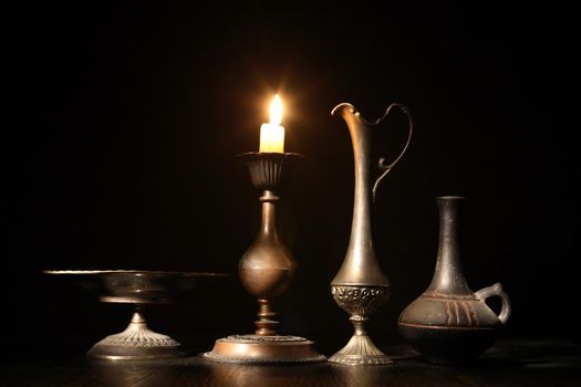 Set of vintage dishes near lighting candle on dark background