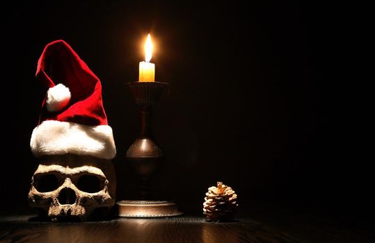 The death of Santa Claus. Human skull with Christmas hat near lighting candle