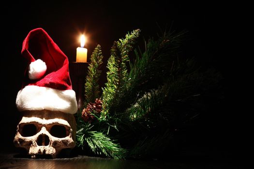 The death of Santa Claus. Human skull with Christmas hat near lighting candle