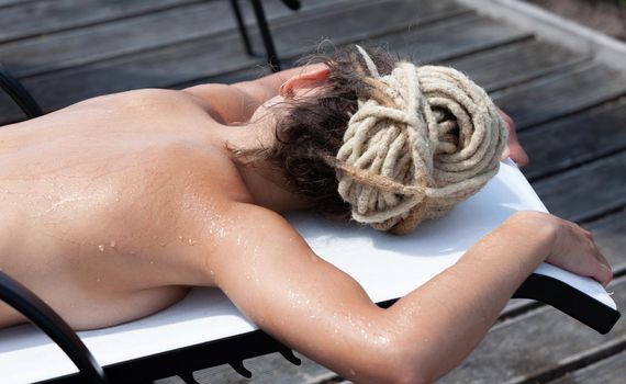 Beauty and healthy lifestyle concept. Naked woman with dreadlocks sunbathing on sunbed near the pool. 