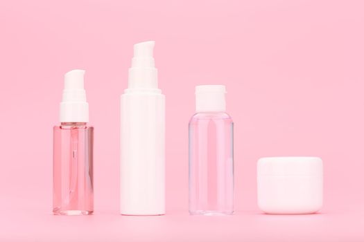 Minimalistic still life with set of unbranded cosmetic bottles with cleansing gel, face cream, lotion and under eye cream against bright pink background