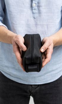 Man's black leather personal cosmetic bag or pouch for toiletry accessory in a men's hands in blue shirt. Style, retro, fashion, vintage and elegance