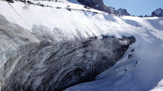 A huge wall of ice. Bogdanovich Glacier in the mountains of Almaty. The wind blows the snow away from the high frozen wave. Unusual shape and color of the ice. Moraine lake in winter in the mountains