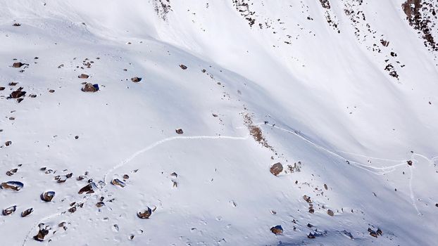 A group of climbers is walking in the mountains. Top view of the trail and the people. Snow-capped peaks, steep cliffs and precipices. A glacier is visible in the distance. Lots of snow. Almaty