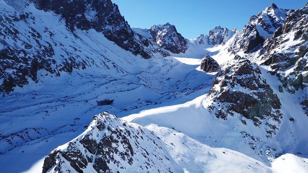 A group of climbers is walking in the mountains. Top view of the trail and the people. Snow-capped peaks, steep cliffs and precipices. A glacier is visible in the distance. Lots of snow. Almaty