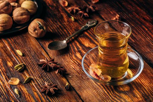 Spiced tea with star anise, cardamom and dried lime in armudu glass over wooden surface