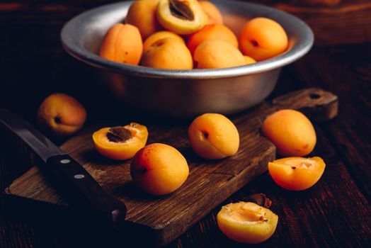 Mellow apricots with knife over old wooden cutting board and metal bowl with fruits