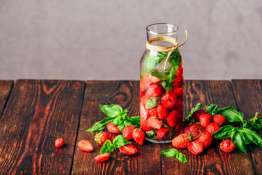 Flavored Water in Bottle with Fresh Strawberry and Basil Leaves. Scattered Ingredients on Wooden Table. Copy Space.