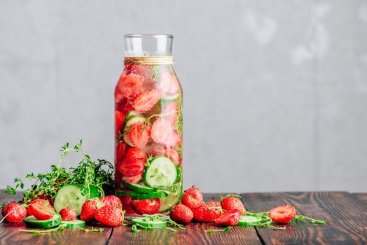 Bottle of Infused Water with Fresh Strawberry, Sliced Cucumber and Springs of Thyme. Ingredients Scattered on Wooden Table. Copy Space.