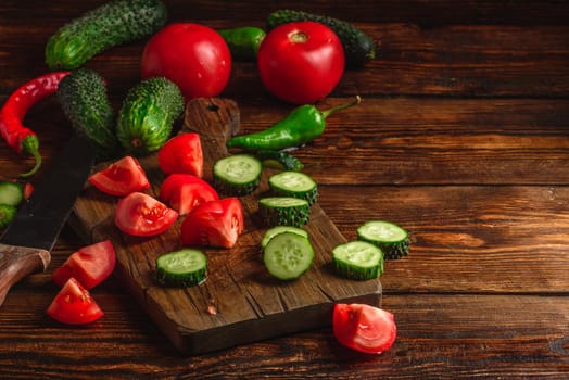 Sliced vegetables. Tomatoes, cucumbers and chili peppers over wooden background.