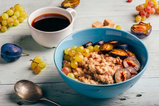 Healthy breakfast concept. Porridge with fresh plum, green grapes and cup of coffee. Ingredients over wooden background.