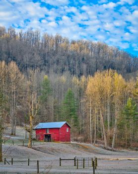 Old red barn with early morning sun rays on trees.