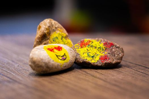 A group of three painted pebbles with emoji faces on a table