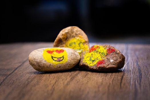 A group of three painted pebbles with emoji faces on a table