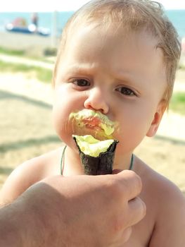 A child eats ice cream on a hot summer day. The father feeds the baby ice cream. The whole face of the child is smeared.